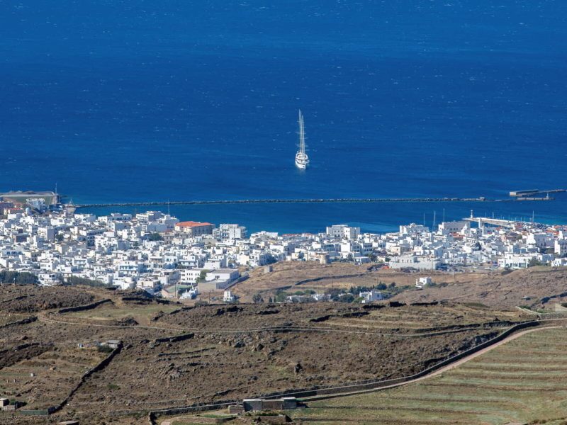 Greece Tinos island Cyclades. Aerial drone panoramic view of Hora town, whitewashed building, port, ship, Aegean vast blue sea, summer vacation.