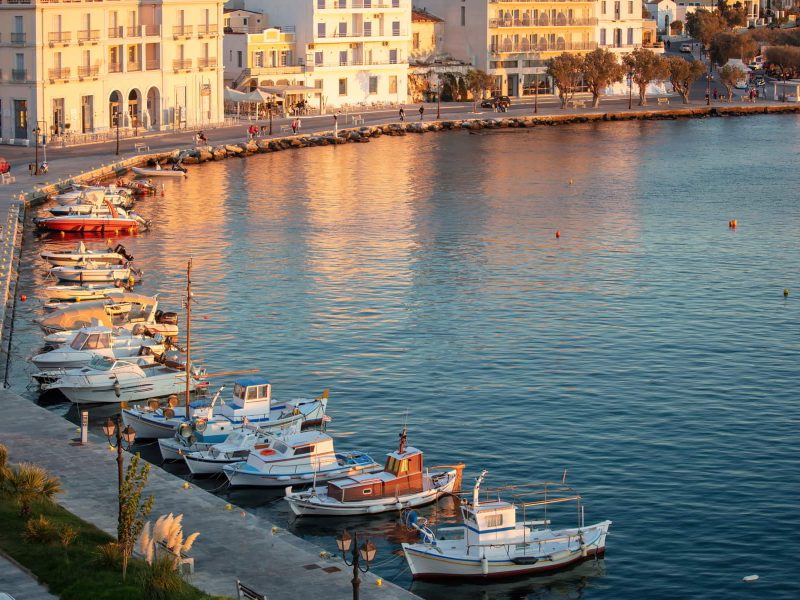 Tinos island Hora town at sunset Cyclades Greece. Above view of port, sun colors gold Aegean sea and building, blue pink sky summer holiday.